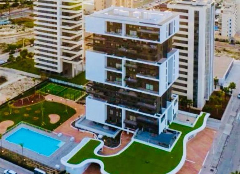 A building with a garden and a pool in Calpe, adjacent to many other buildings.