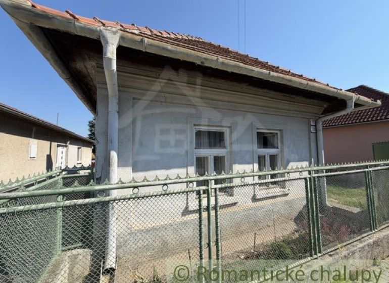 A family house in Šurany with white windows and a red roof behind a fence.