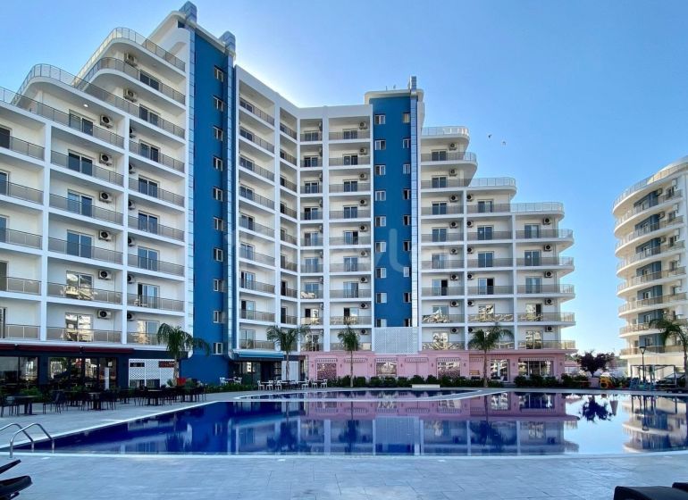 Residential complex in Iskele with a swimming pool, surrounded by tall buildings and palm trees.
