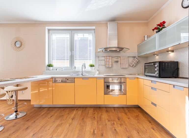 A bright kitchen with orange cabinets and a wood-patterned floor in a three-room apartment.