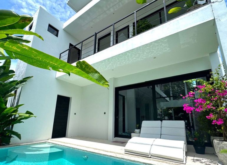 Bali villa with a pool and terrace, surrounded by greenery and flowers.