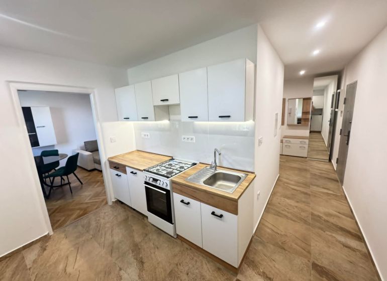 A kitchen in a 2-room apartment with tiles and a wooden decor on the cabinets.