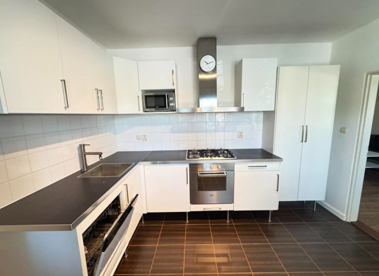 A kitchen in a 3-room apartment with white cabinets and a dark countertop.