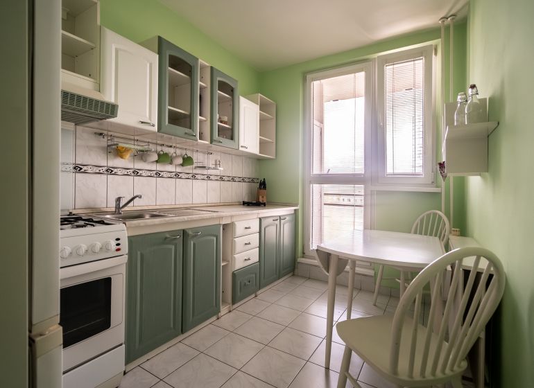 A kitchen in a 3-room apartment with white appliances, a green wall, and a dining table.