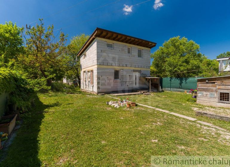 A cottage in Bernolákovo surrounded by green trees, with a spacious lawn and blue sky.
