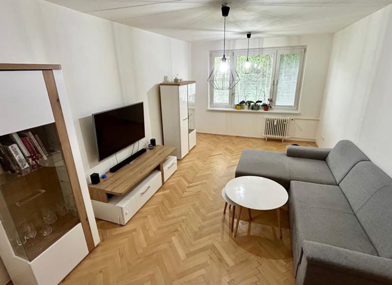 Living room with wood-patterned flooring, gray sofa set, and television in a three-room apartment.