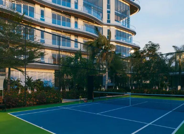A tennis court in front of a modern building in Paje surrounded by greenery and palm trees.