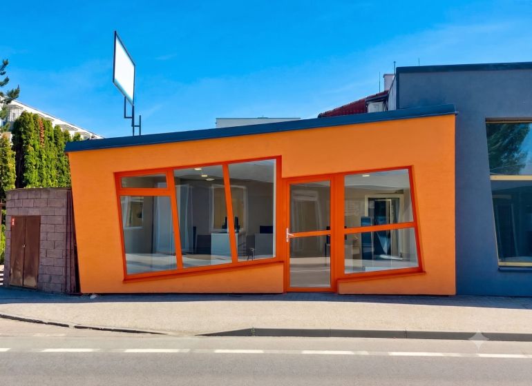The orange facade of commercial spaces on Zlatovska Street in Trenčín with large glass windows.