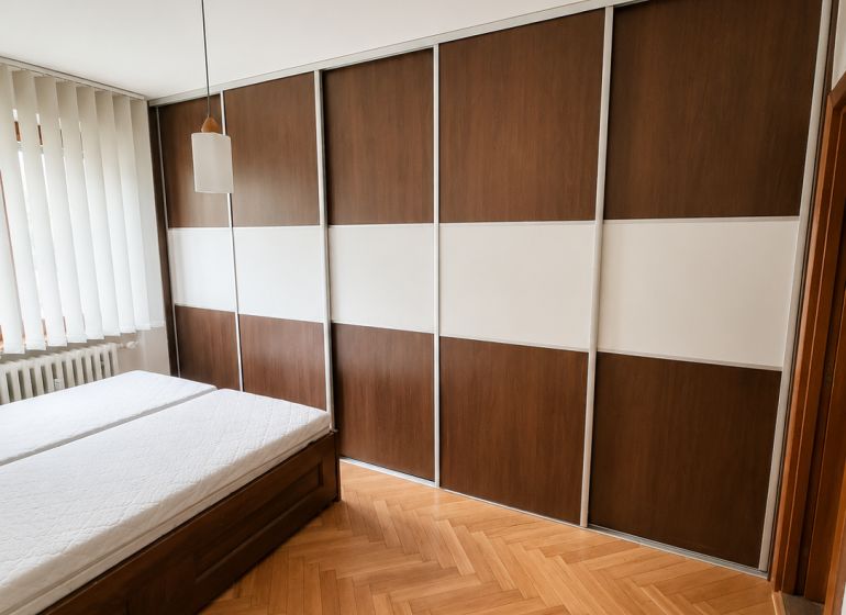 Bedroom with a sliding wardrobe, bed, and wooden decor flooring in a 2-room apartment.