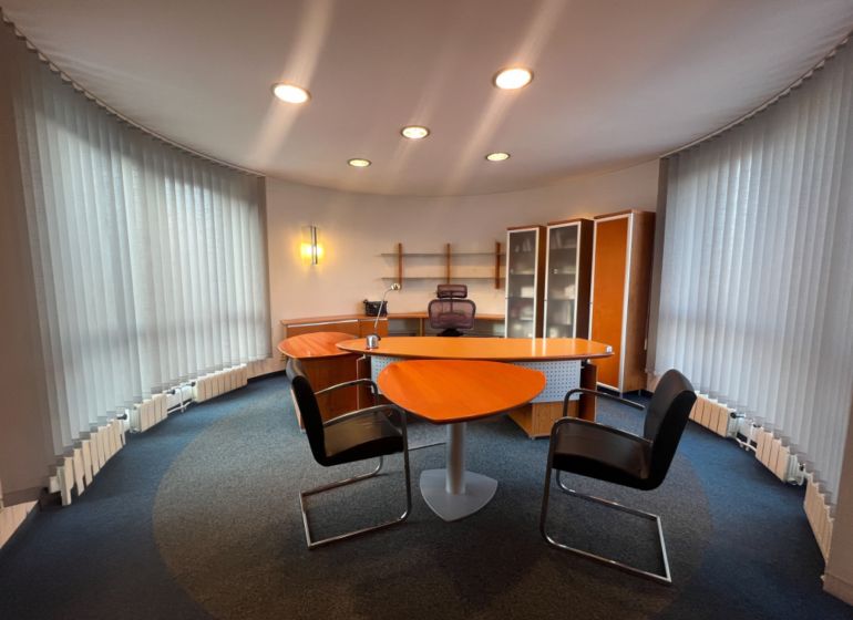 An office with a wooden decor desk, shelves, and illuminated vertical blinds.