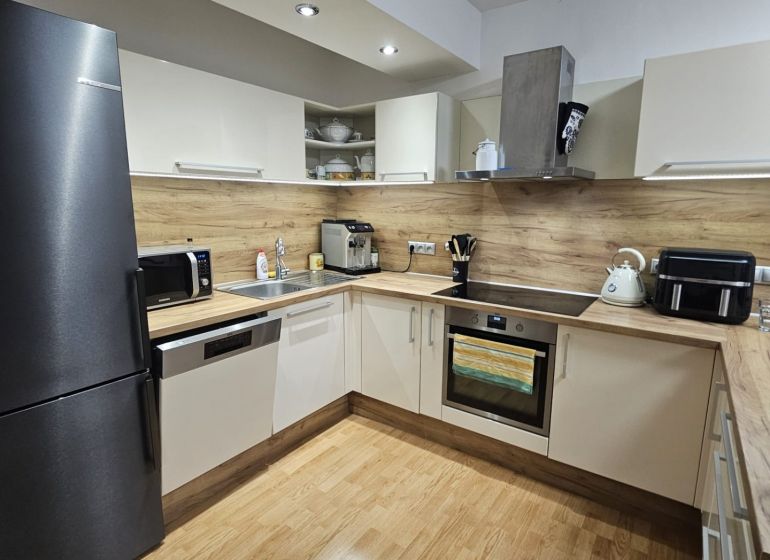 A kitchen in a 3-room apartment with a wood-patterned floor and modern appliances.
