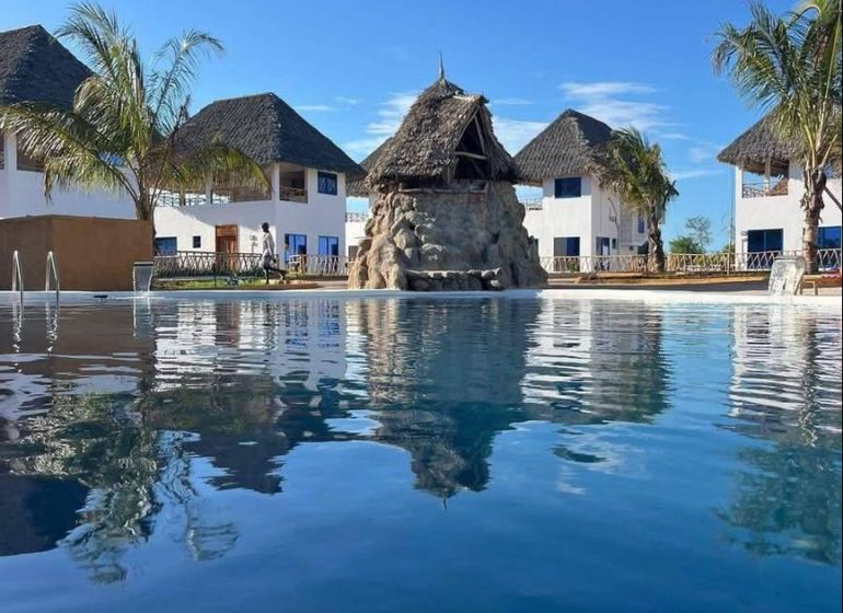 A family house in Zanzibar surrounded by palm trees by the pool under the blue sky.