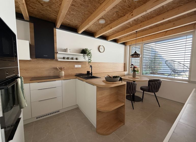 A kitchen in a family house with a wooden decor floor, wooden beams, and a dining table.