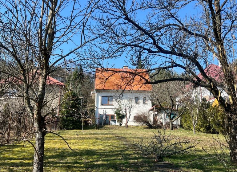 A family house in Podháj, Kráľová, surrounded by trees and lawn, with an orange roof.