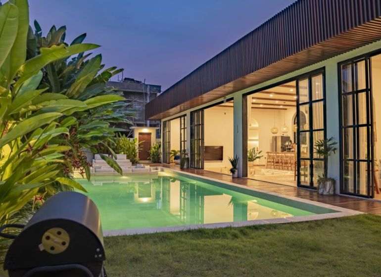 Villa in Bali with a lit pool, terrace with wooden decor, and garden.