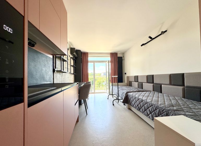 Studio apartment with a kitchenette and two beds, flooring with a wooden appearance.