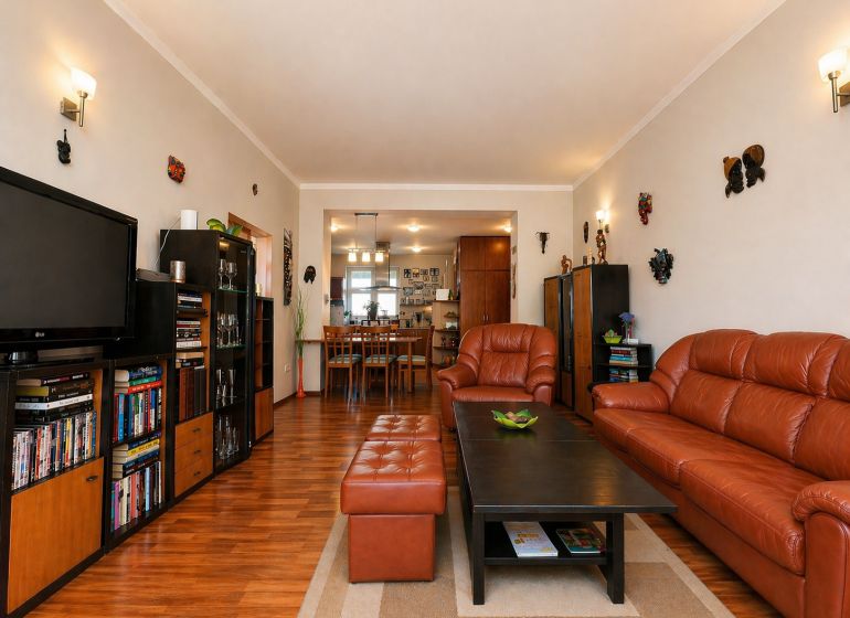 Living room in a 4-room apartment with a wooden decor floor and a brown sofa.