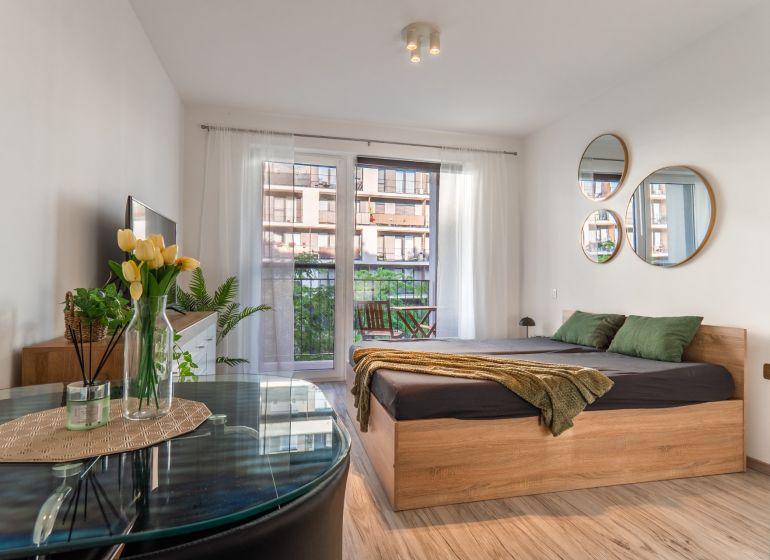 Bright 1-room apartment with a bed, mirrors, and wooden decor flooring, balcony outside the window.