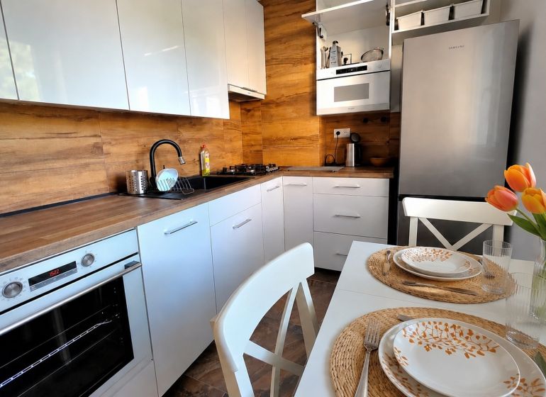 A kitchen in a 2-room apartment with white cabinets, a wood-patterned floor, and a table with flowers.