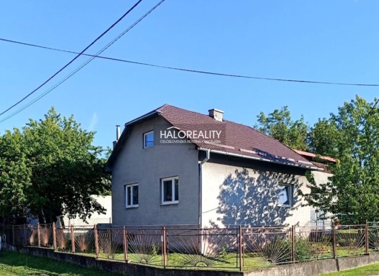 A family house in Margecany with a sloped roof, fenced, surrounded by greenery and a blue sky.