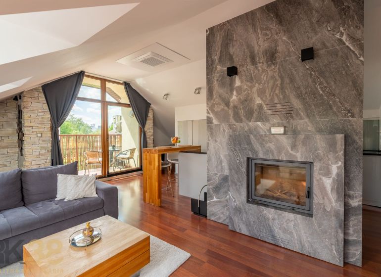 Living room of a 3-room apartment with a sloped ceiling, fireplace, and wood-patterned flooring.