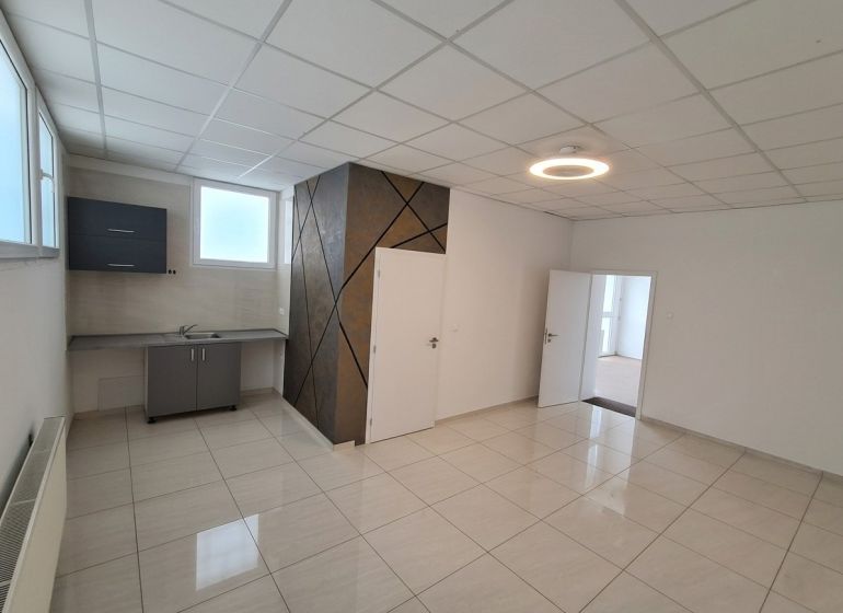 An office space with a kitchenette and a light floor with a wall decoration.