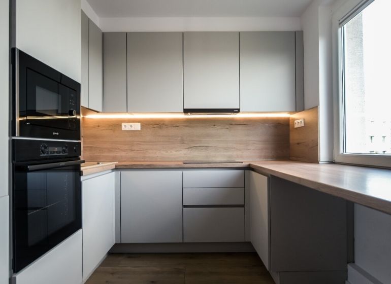A kitchen with built-in appliances, light cabinets, and a wood-patterned floor in a three-room apartment.