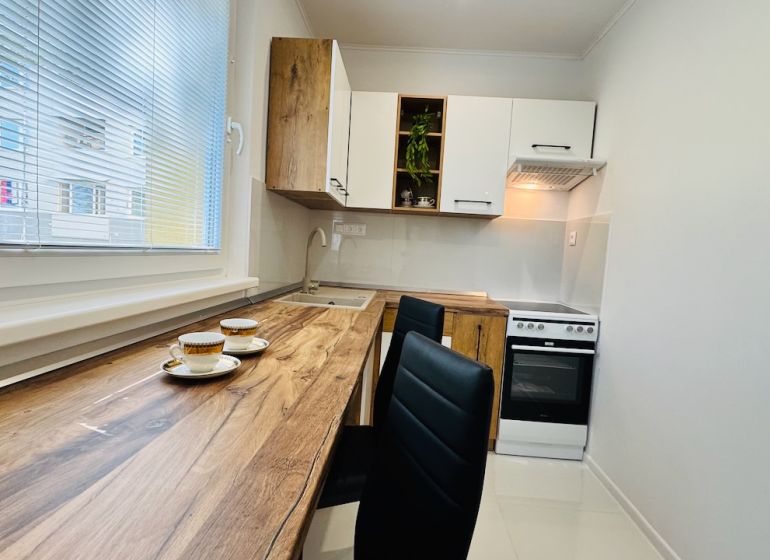 A kitchen in a studio apartment with wood-patterned flooring, white cabinets, and appliances.