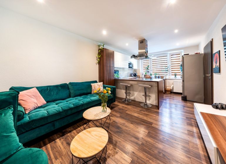 Living room with a kitchenette in a 3-room apartment, wooden decor flooring, green sofa.