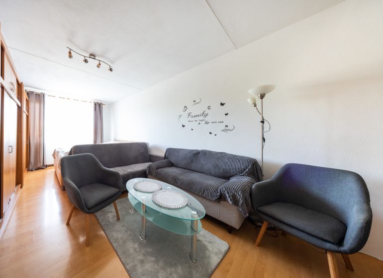 Living room with wood-patterned flooring in a 3-room apartment, gray sofas, glass table.