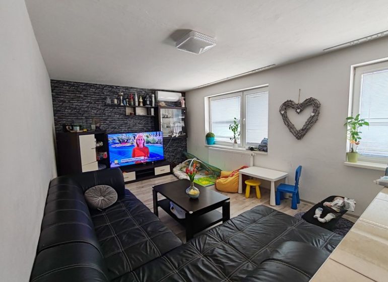 Living room in a three-room apartment with a sofa and TV, floor with wood decor.