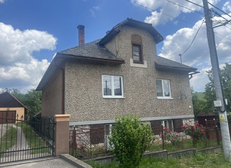 A family house in Rudná with a two-story facade, a fenced plot, and a blue sky.