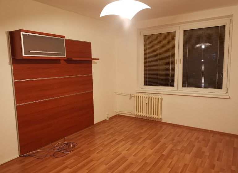 A room with a wooden decor floor, white walls, and a wall cabinet in a 3-room apartment.