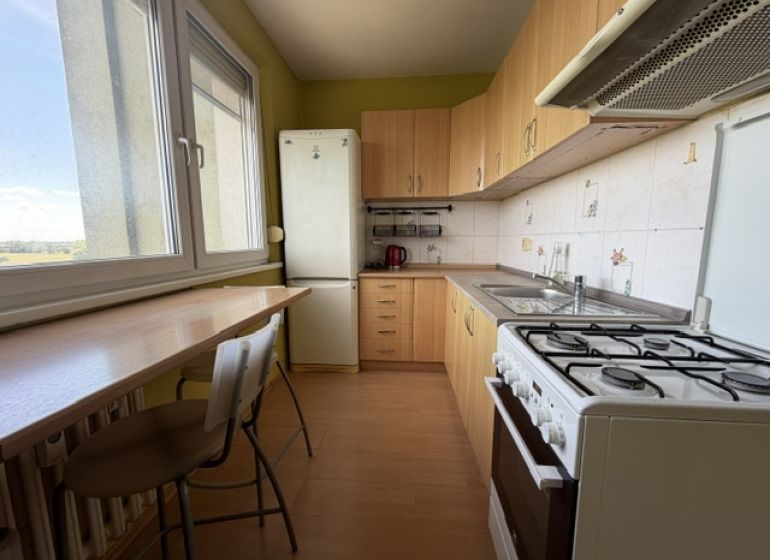 A kitchen in a studio apartment with a wood-patterned floor and light-colored furniture.