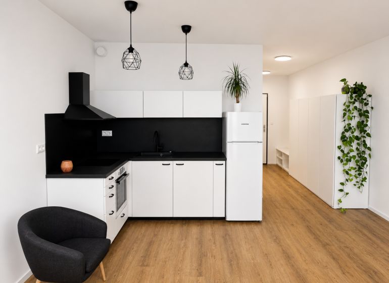 A kitchen in a studio apartment with white cabinets, black details, and a wood-patterned floor.