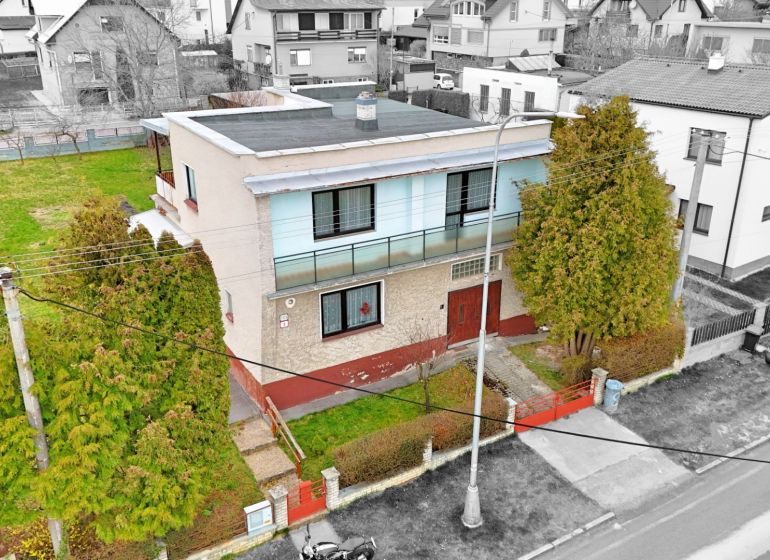 A two-story family house in Martin with a garden, surrounded by trees and a fence.