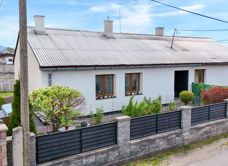A family house in Košťany nad Turcom with a garden, fence, and ornamental shrubs.
