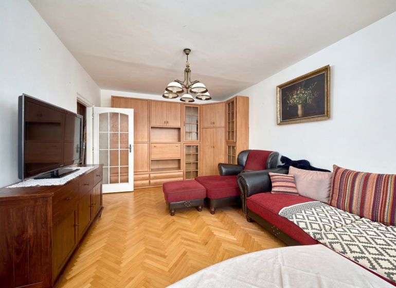 Living room in a two-room apartment with a red sofa, TV, and wooden decor flooring.