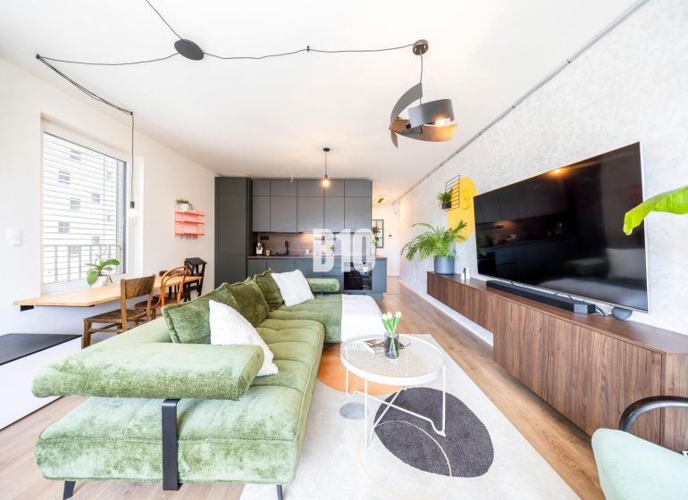 Living room in a three-room apartment with a wooden decor floor, a green sofa, and a television.
