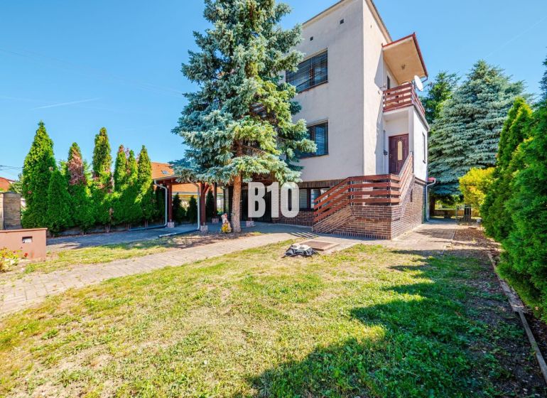 A family house in Branč with greenery, a terrace, and wooden details on the railing.