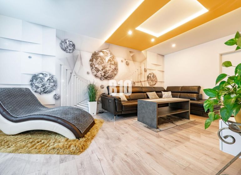 Living room of a three-room apartment with a comfortable sofa and a wooden-patterned floor.