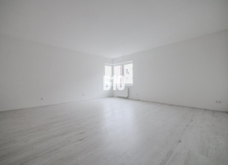 Empty room in a studio apartment with wood-patterned flooring.