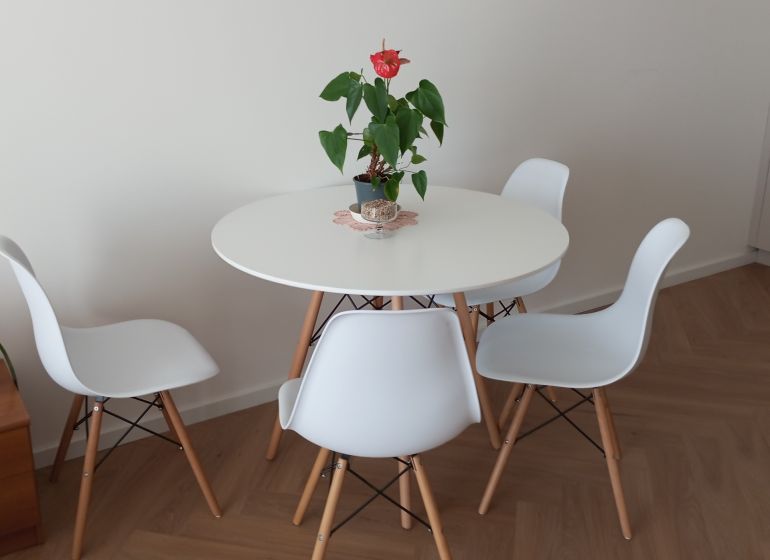 A round table with white chairs on a wooden floor in a 2-room apartment.