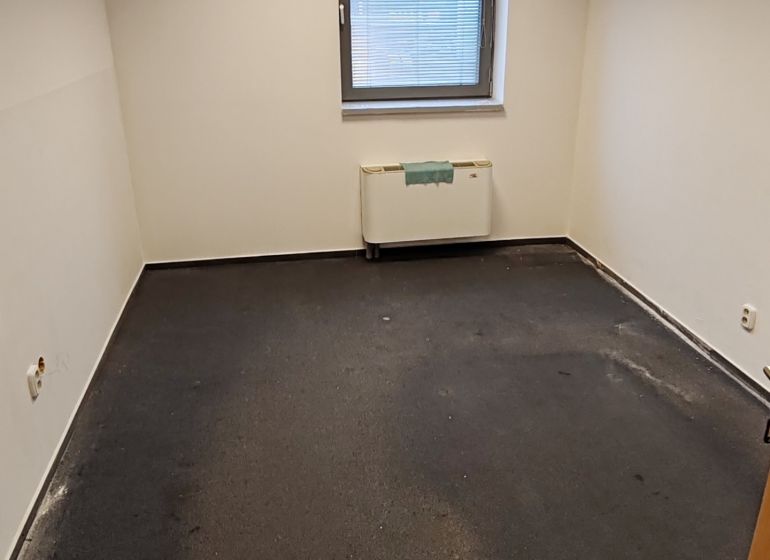 Interior of an office with a window, radiator, and dark-colored flooring.