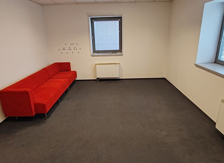 A red sofa in an office with a window and a radiator, dark decor flooring.