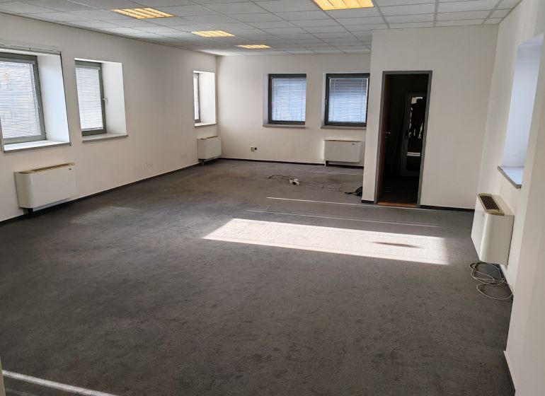 Offices with windows and carpet, bright walls and ceiling lighting.
