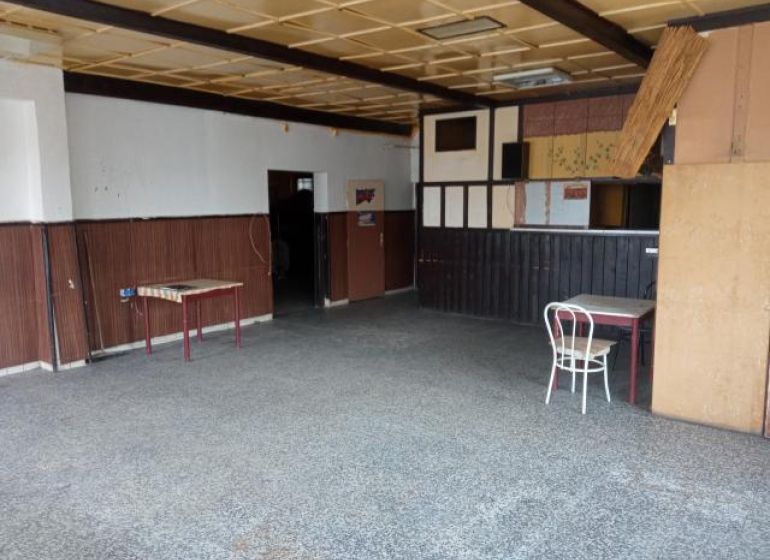 The building has old tables, a chair, wall paneling, and a stone floor.