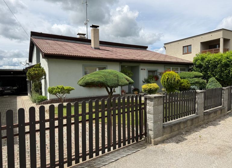 A family house in Chrabrany with a landscaped garden, fence, and driveway.