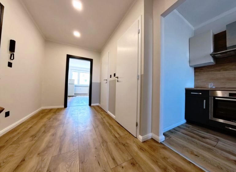 A hallway in a 3-room apartment with a wooden decor floor and an entrance to the kitchen.