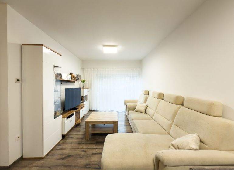 Living room in a 3-room apartment with a light sofa, wooden decor flooring, and a TV stand.